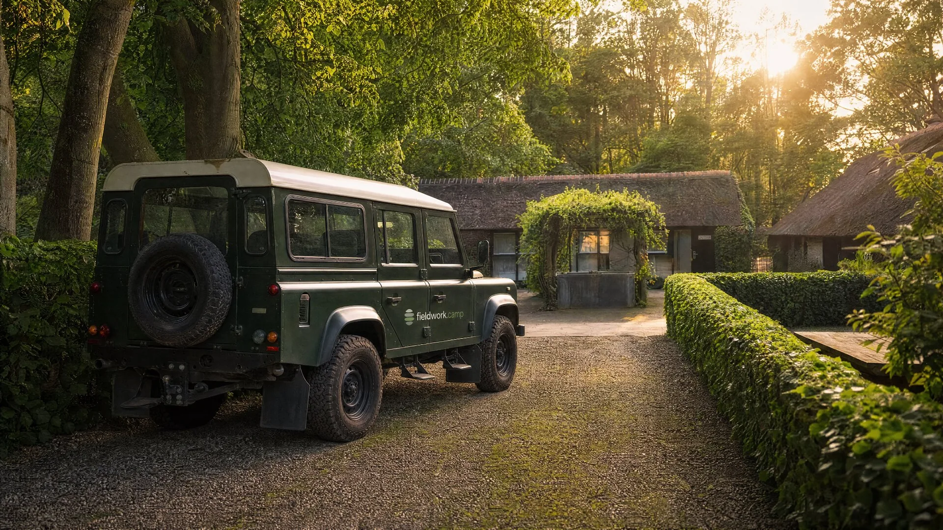Groene Land Rover Defender met fieldwork.camp op de deur, op het erf van Tussen de Velden