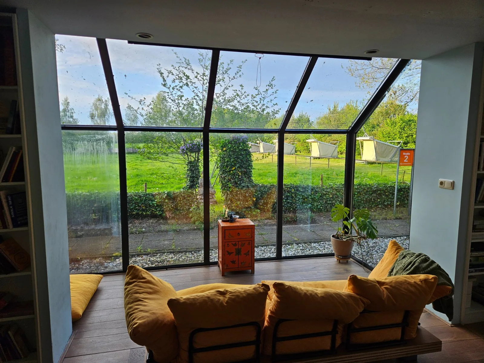 De studio met glaswand en uitzicht op het veld met de tenten