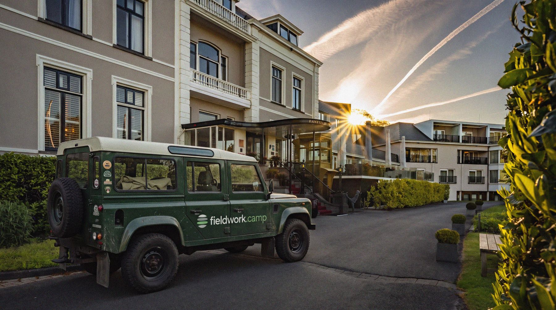 Groene Land Rover Defender met fieldwork.camp op de deur, voor de ingang van Landgoed Lauswolt